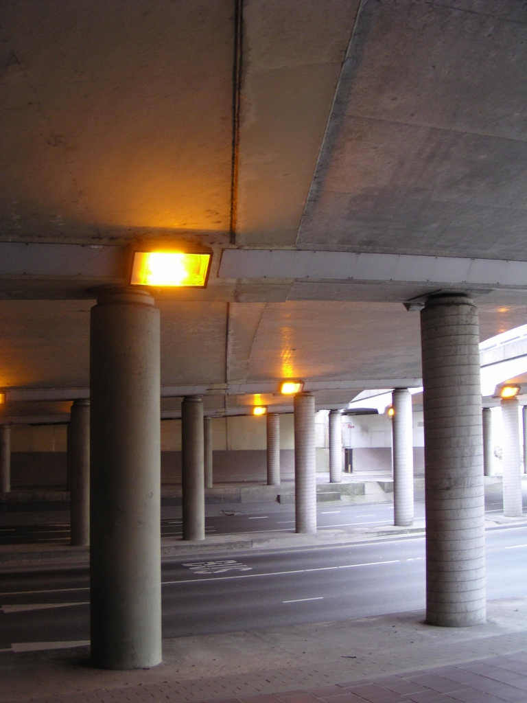 p4300037.jpg - Veel van het bij de vorige foto's opgehangen verhaal over de Beatrixbruggen kan worden herhaald bij KW 13, de viaducten in de aansluiting Veldhoven. Ook hier een verbreedsel aan het oorspronkelijke creme-witte jaren zestig viaduct. De noodzaak was hier duidelijk: halfklaverblad bogen voor completering van de aanvankelijk als halve aansluiting uitgevoerde afrit Veldhoven moesten over het viaduct lopen voor in- en uitvoegen van/naar de richting Maastricht. De creme afwerking werd achterwege gelaten bij het verbreedsel, en het spiraal motief op de steunen verraad een moderne bekistingstechniek met sonotube. Ook deze verbredingen hebben er jaren ongebruikt bijgelegen na de bouw van de aparte af/toerit viaducten. Bij de spitsstrokenaanleg begin deze eeuw werd de aanwezige ruimte en asfalt dankbaar hergebruikt voor  pechhavens .