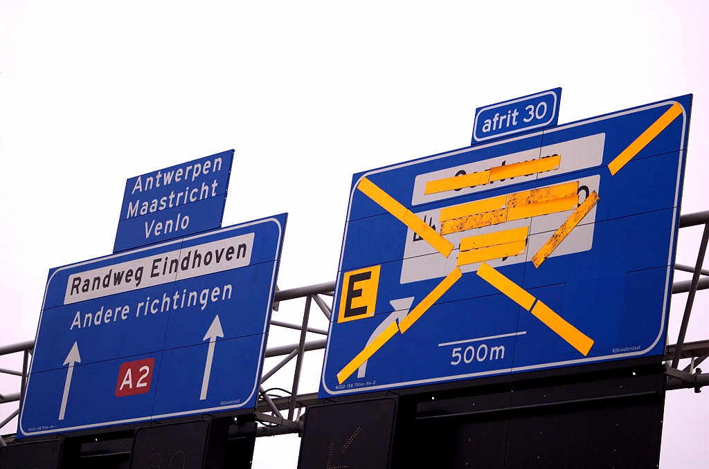 20081130-153302.jpg - Op het rechtdoorbord de gebruikelijke bijruitering van vergelegen doelen, die in de eindsituatie weer verdwijnt, evenals de overplakker over het N2 wegnummerschildje. Lange pijlen geven conform de VNB (vernieuwing bewegwijzering) aan dat beslismomenten nog even op zich laten wachten. Ondanks de gele afplakkers (magneten?) op het andere bord kunnen we wel raden wat er op staat: Centrum, industriesymbool met nummers en Strijp. Eigenlijk zou dit portaal zich op 600 meter van de afrit Strijp moeten bevinden, maar zou dan zo'n beetje op KW 9 (aansluiting Airport) terechtkomen. Vandaar de afwijkende afstand van 500 meter.