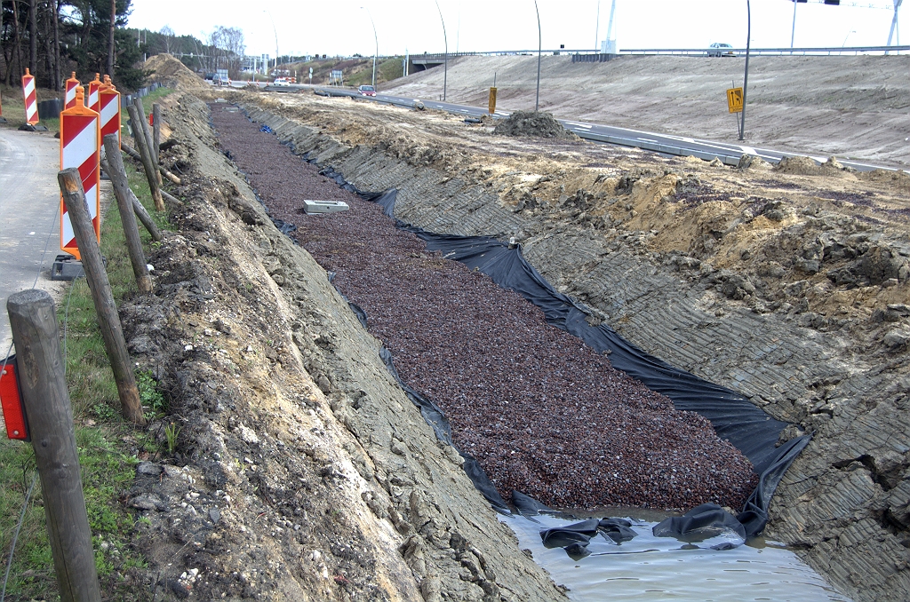 20100405-150419.bmp - Bodem van de bermsloot wordt voorzien van folie en een soort lava-achtige steentjes. Misschien een zuiveringsvoorziening voor afstromend hemelwater, alvorens het in de bodem wegzakt.