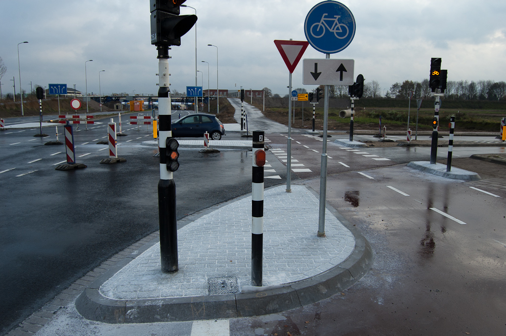 20111127-144754.jpg - In de toeleidende wegen naar de Hovenring is ook hard gewerkt. Zo zijn de verkeersgeleidingseilanden in de kruising Grasdreef-Grassteppe afgevuld met beton met print. Aardige details hier voor de liefhebber, zoals de afwijkende asmarkering op het fietspad, de uithollingen overdwars, het verouderde model aanmeldknop zonder terugmelding, en de conflicterende voorrangsaanduidingen tussen het fietspad met bord B6 en de rijbaan met haaietanden.  week 201146 